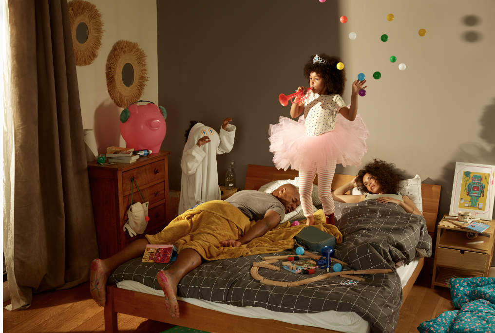 Couple couché sur un lit, épuisés, avec une petite fille sautant sur le lit
